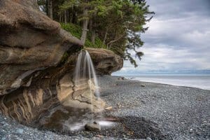 A small waterfall spills onto the stony Sandcut Beach