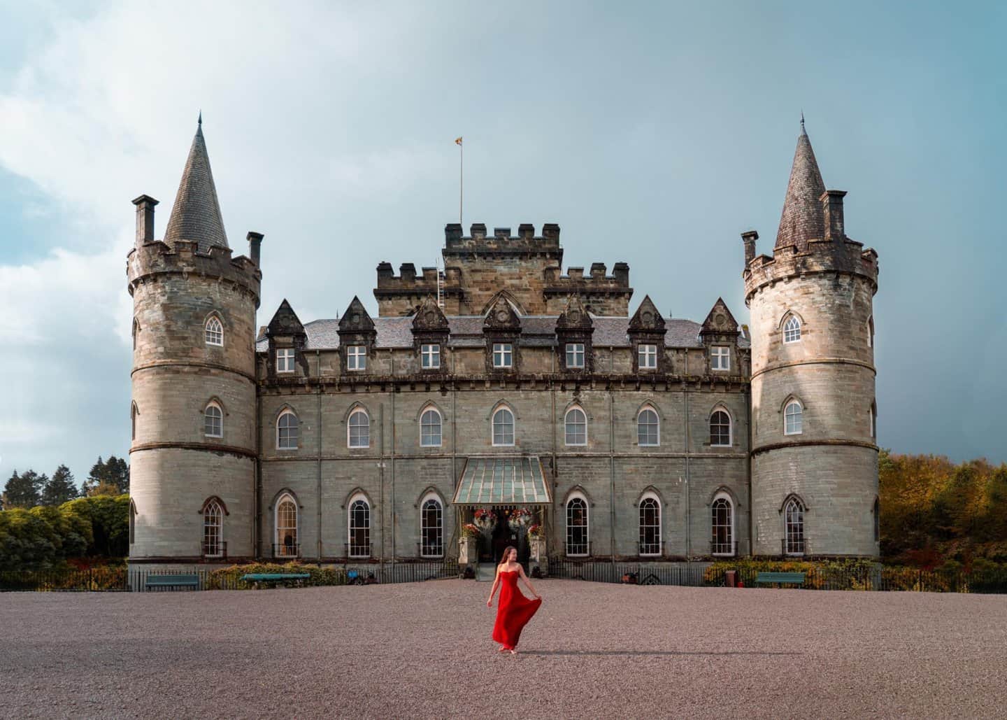 A woman in a red dress poses in front of Inveraray Castle in Scotland.