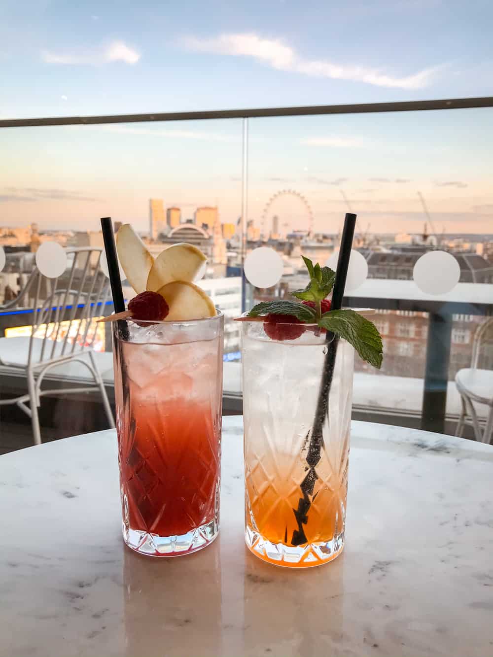 Two cocktails on a table at Hotel Indigo Bar in Leicester Square, with the London Eye and other London landmarks in the background.