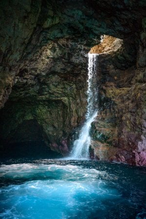 Kauai landscape photography featuring a waterfall spilling into a sea cave on the NaPali coast.