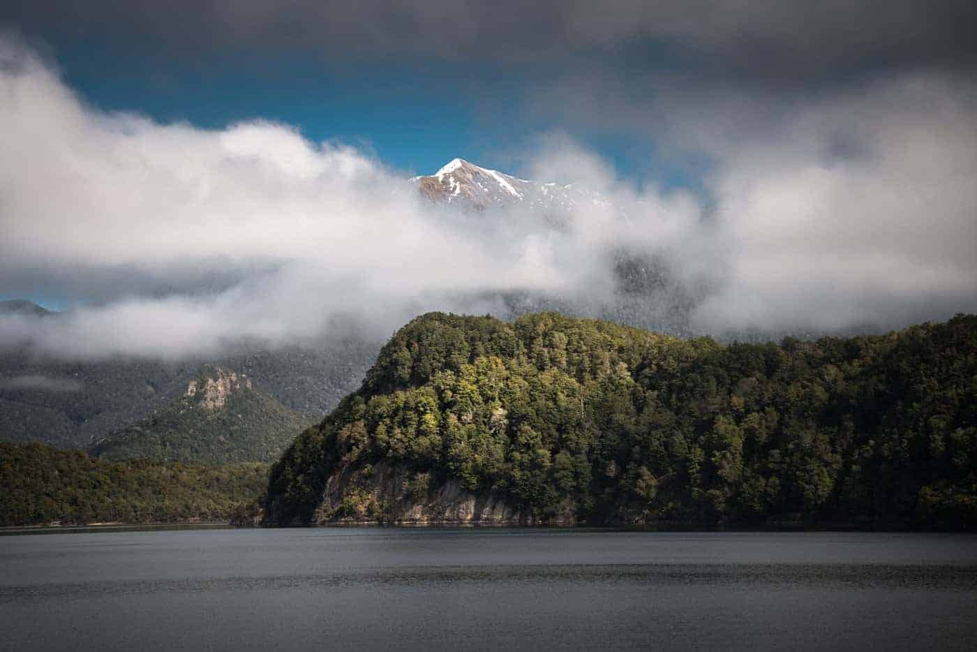 The clouds disperse revealing snow capped mountain peaks on the Doubtful Sound.