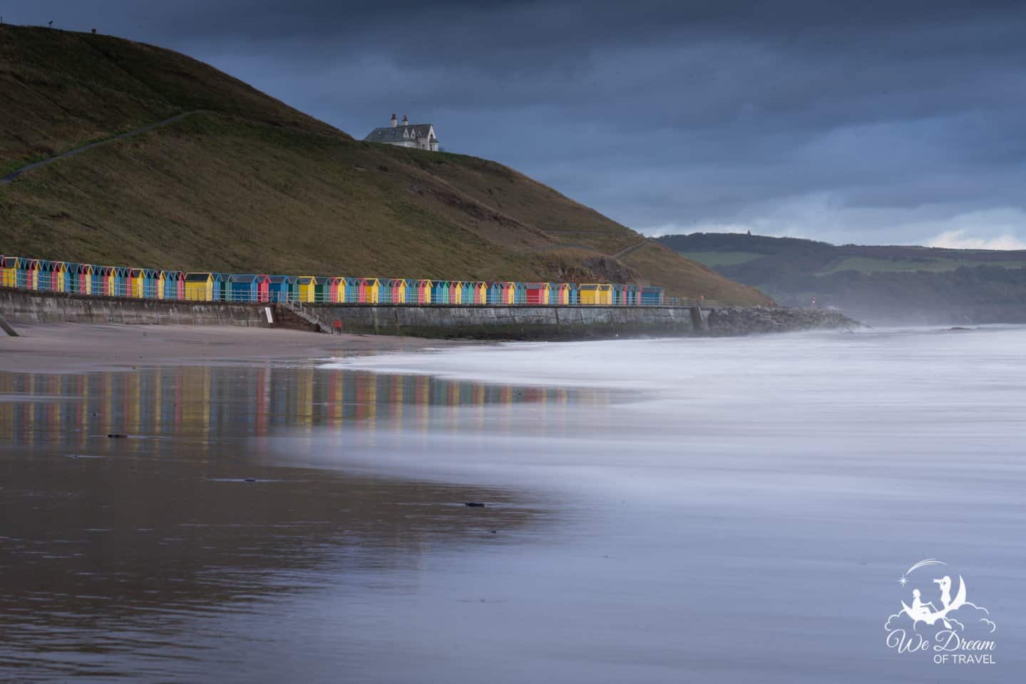 Long exposure photograph of Whitby Sands beach with colourful beach huts lining the seafront.