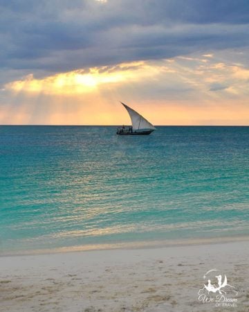 A traditional dhow sails just off the shore of Zanzibar at sunset.