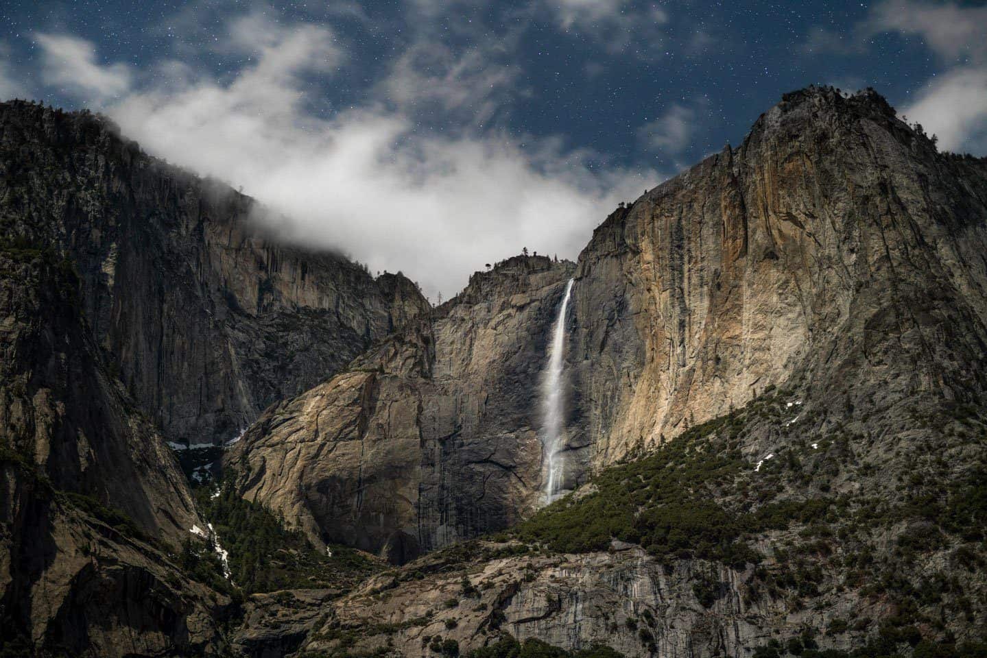 A night photo of Upper Yosemite Falls being lit by moonlight.