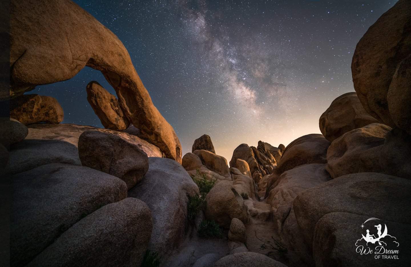 The otherworldly rock formations of Joshua Tree bathe in moonlight while the Milky Way rises in the distance.