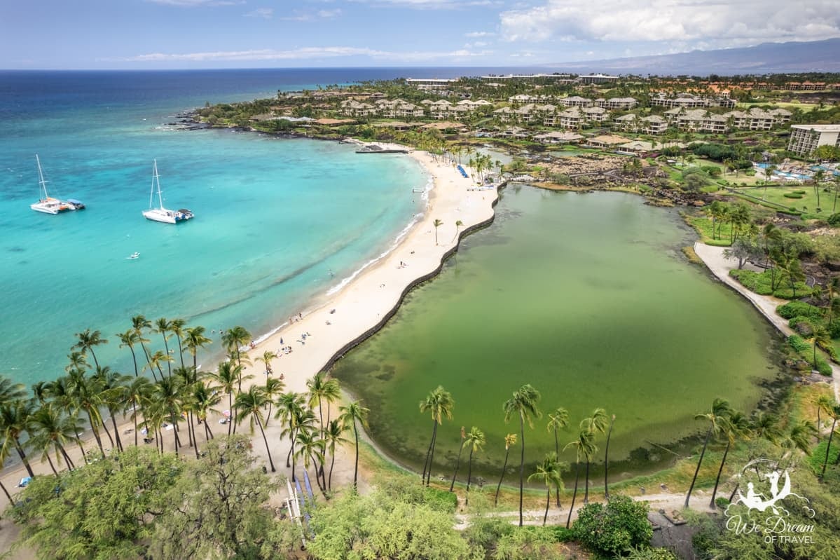 Drone photo showing palm trees lining the lagoon, beach, and shoreline of Waikoloa in Kona on the Big Island.