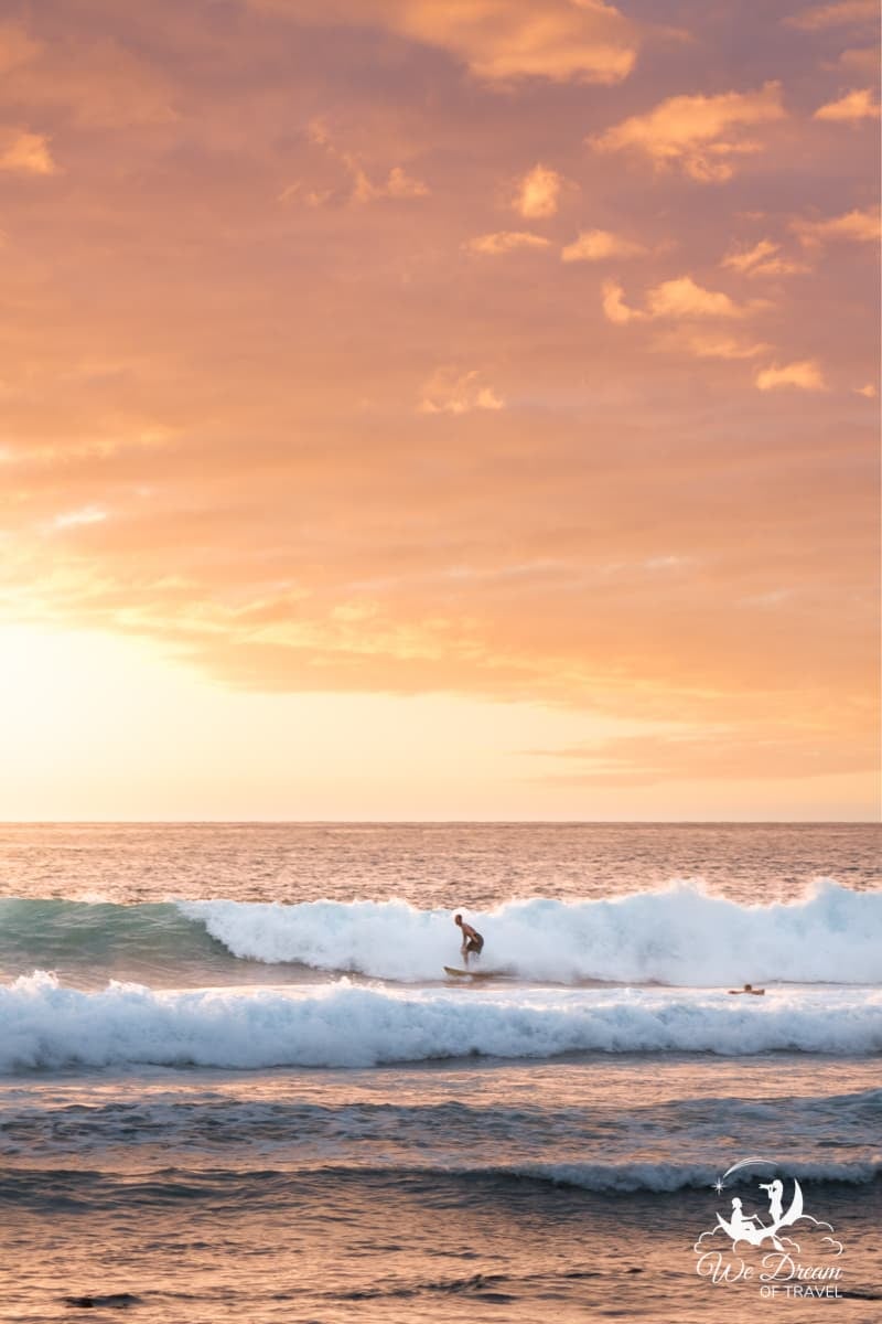 A surfer rides the waves at Pine Trees Beach during a magical sunset on the Big Island.