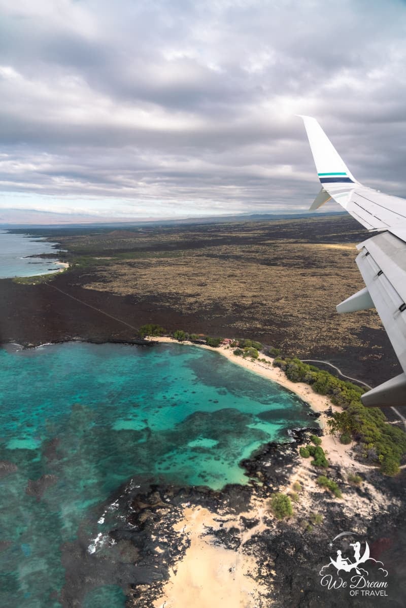 A photo from an airplane window looking out over a beach on Kona flying over the Big Island of Hawaii.
