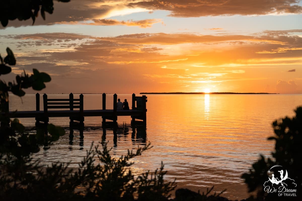 A couple sat on a dock looking out towards the sun setting over the ocean in Key Largo, Florida Keys