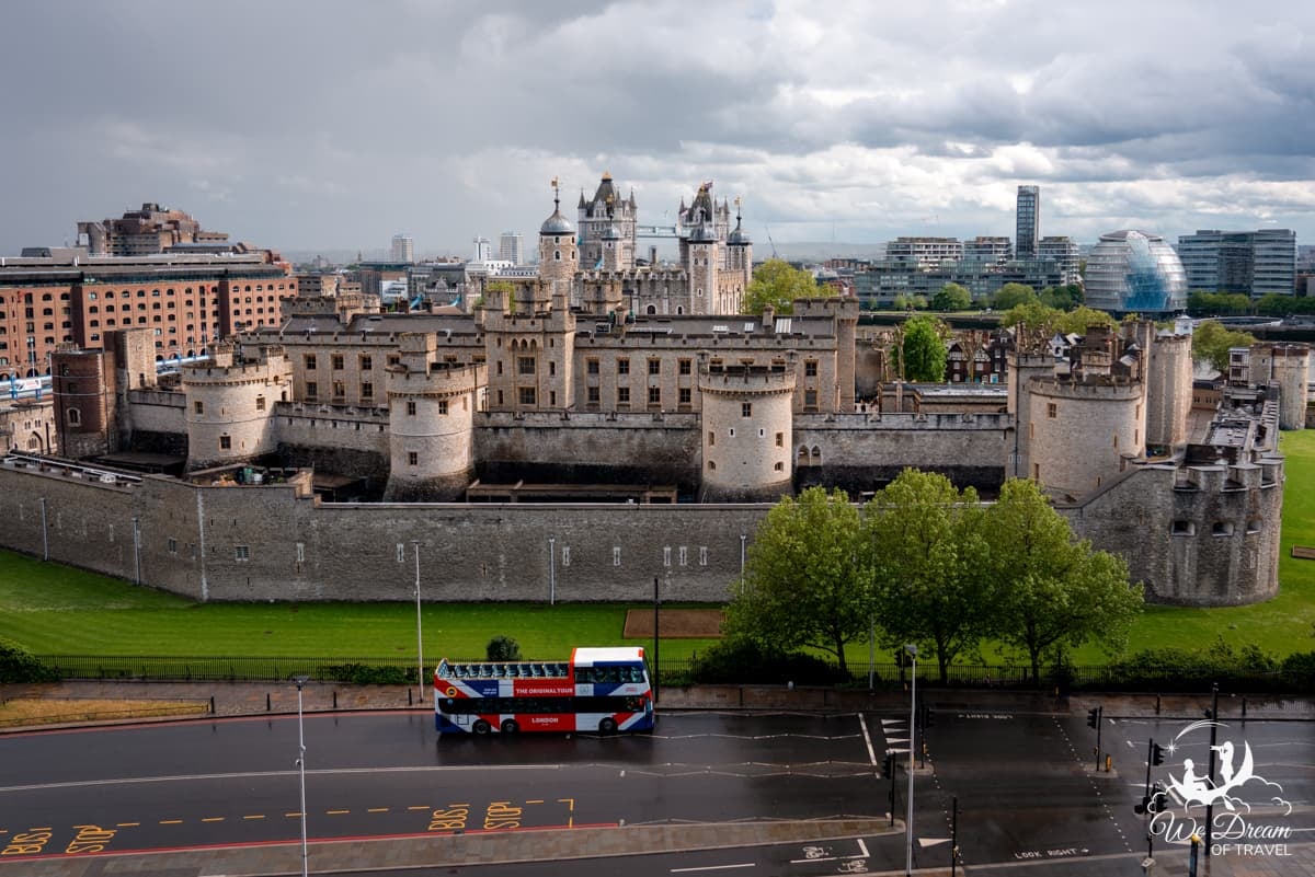 Golden light spills onto the Tower of London and Tower Bridge on an otherwise grey, rainy day in London. As seen from a nearby high-rise building.