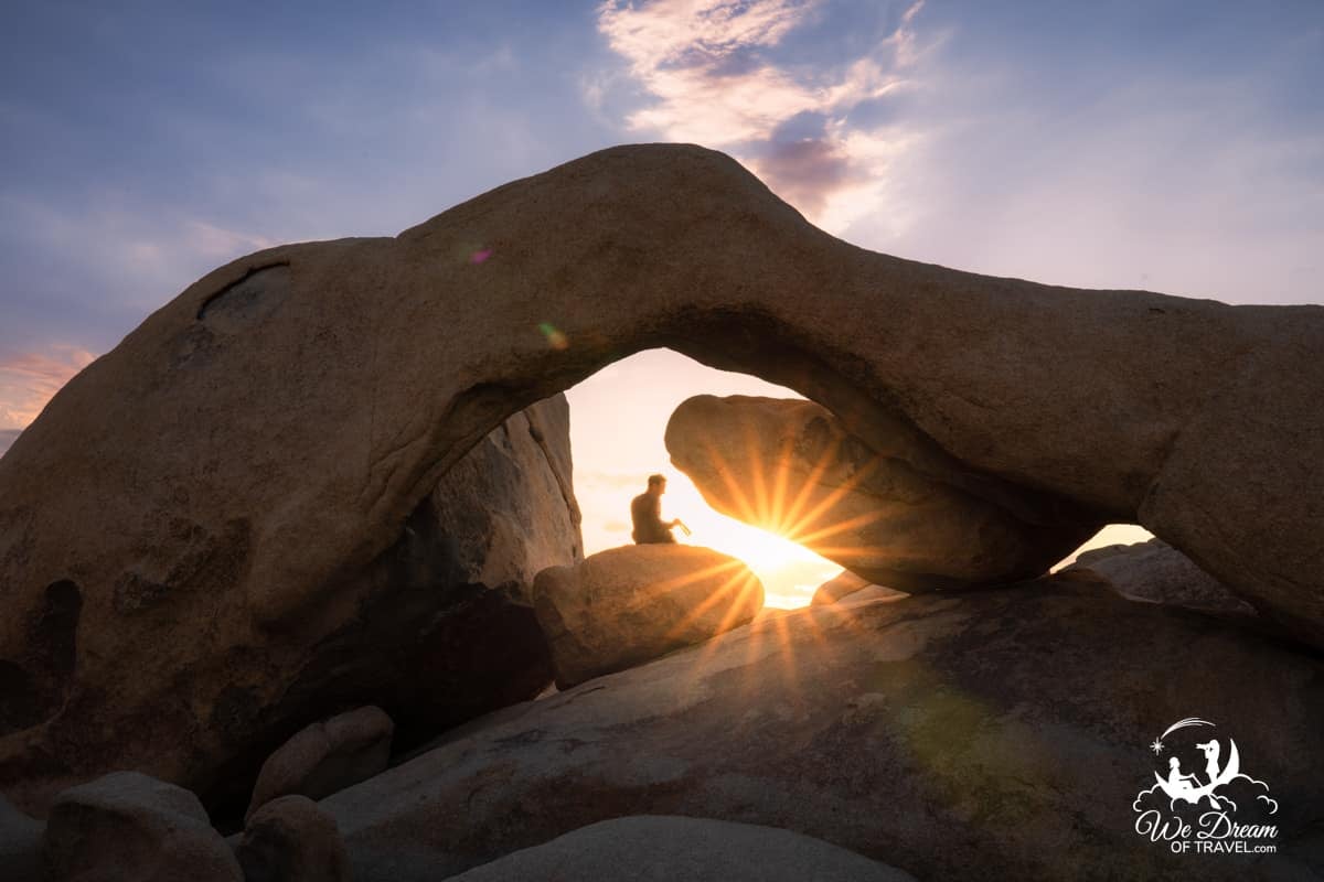 A silhouette sits underneath Arch Rock as the sun rises to begin a one day itinerary in Joshua Tree National park.