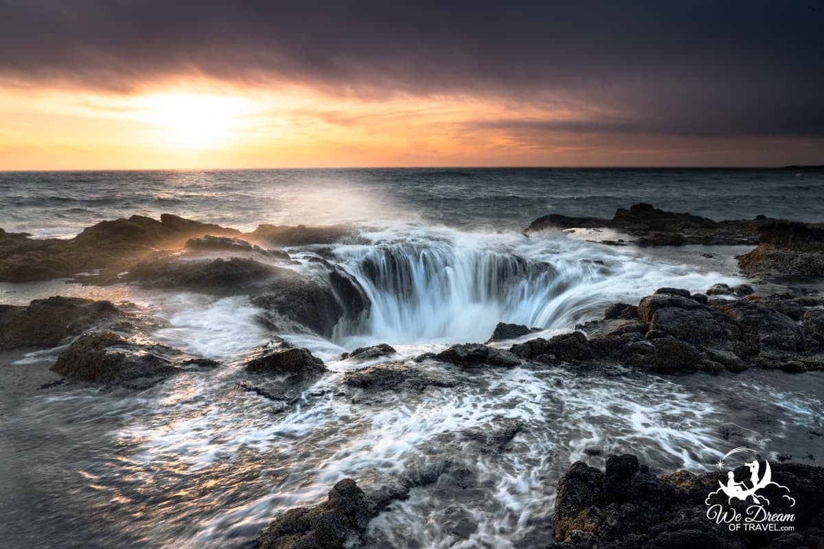 Water draining into Thors Well on the Oregon coast at sunset with a dramatic golden sky under dark clouds.