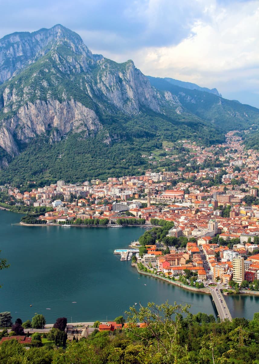 Aerial view of Lecco in Lake Como showing orange roofed houses nestled at the base of a mountain along the side of Lake Como.