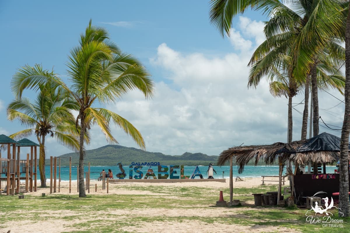 Palm trees sway over Playa Isabela in Galapagos with the welcome to Isabela sign displayed in Puerto Villamil.