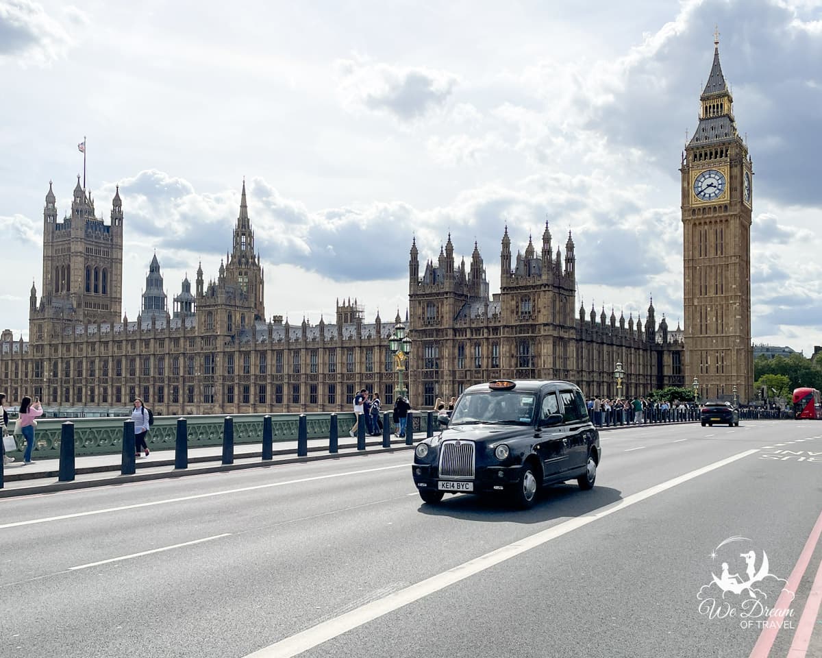 An iconic black taxi driving on Westminster Bridge in front of Big Ben and the Houses of Parliament.